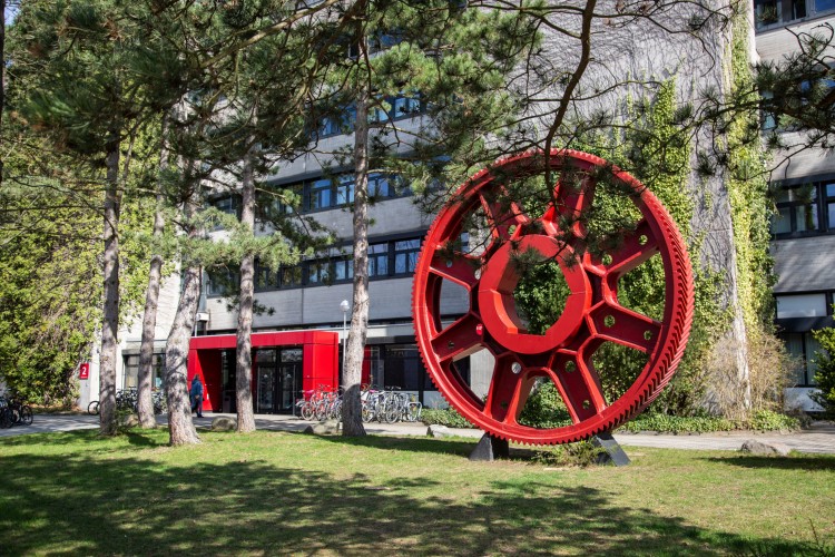 Das rote Zahnrad vor dem Maschinenbaugebäude mit dem Foyer im Hintergrund